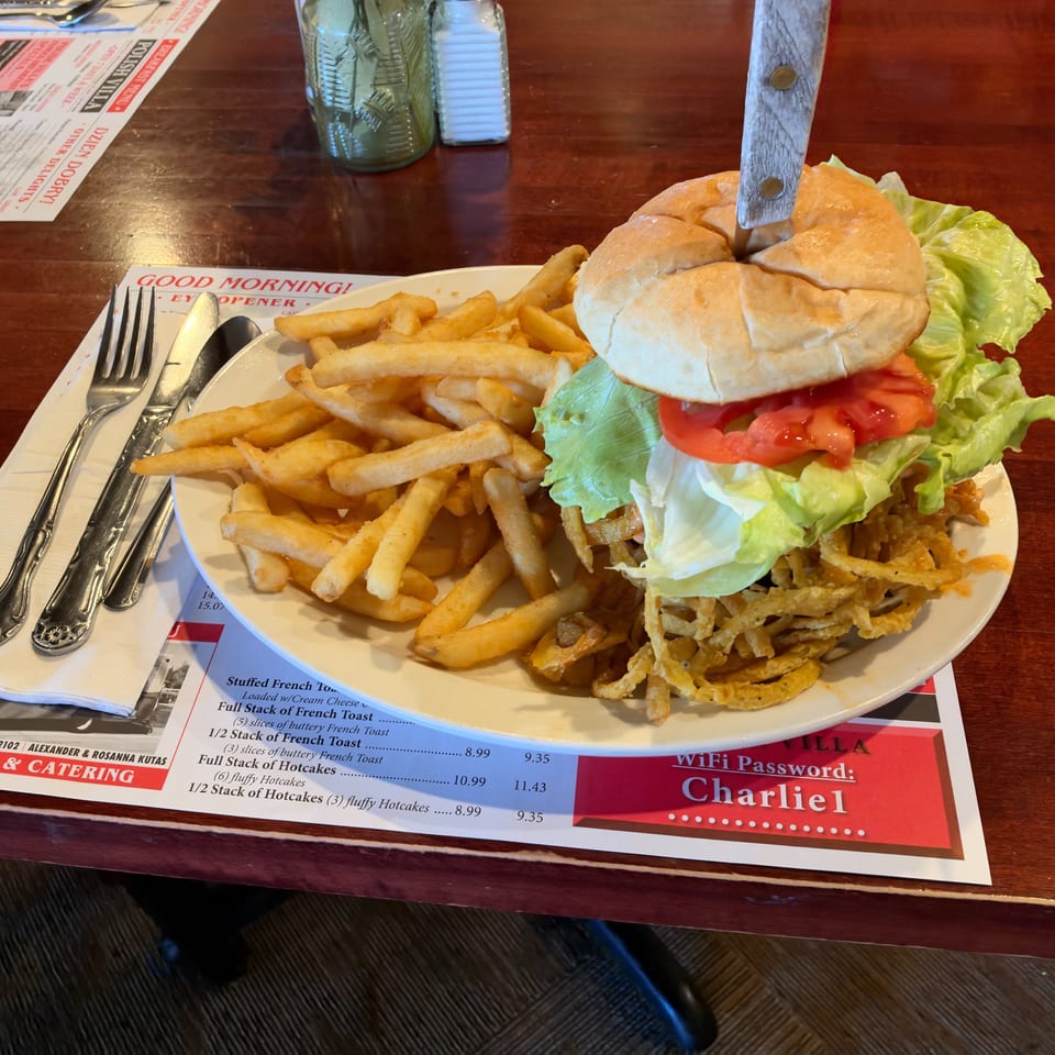 Burger topped with lettuce and tomato, served with French fries and crispy onion strings on a restaurant table.