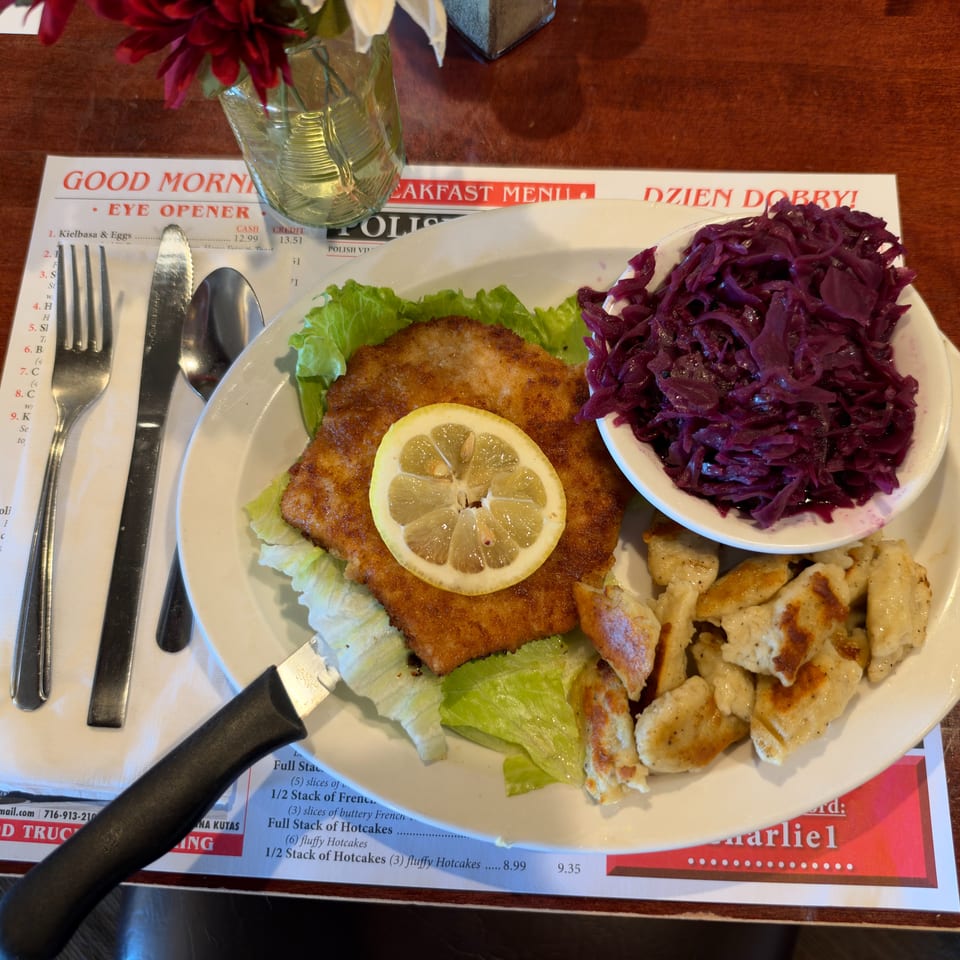 Polish-style meal featuring a breaded cutlet with lemon, red cabbage, and browned dumplings on lettuce.