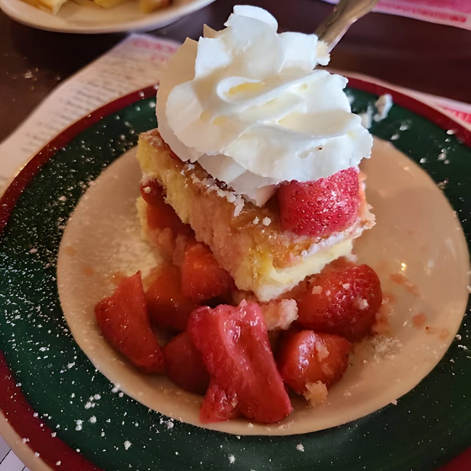 Polish strawberry shortcake with whipped cream and powdered sugar on a green and red plate.