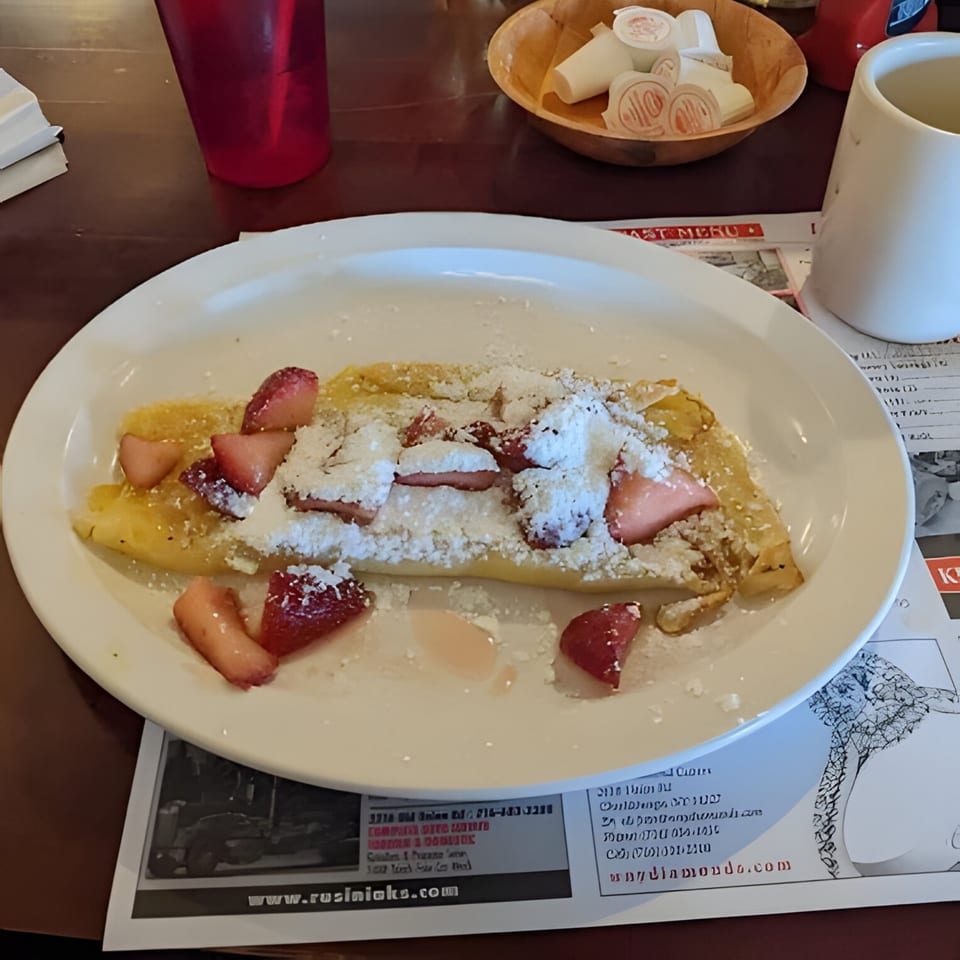 A Polish Villa strawberry and powdered sugar crepe on a white plate with a red cup and creamer.