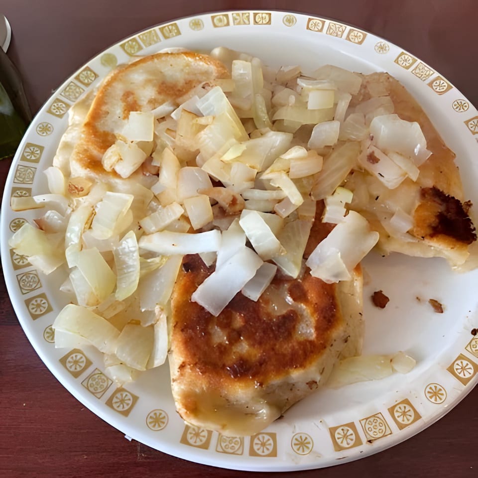 Golden-brown Polish pierogi topped with a generous serving of sautéed onions on a white plate.