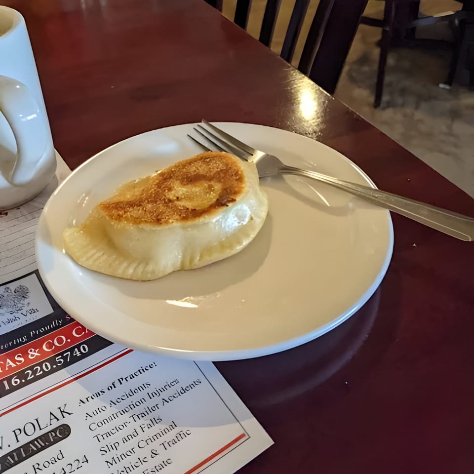 A golden-brown pierogi rests on a white plate with a fork, on a dark red table.