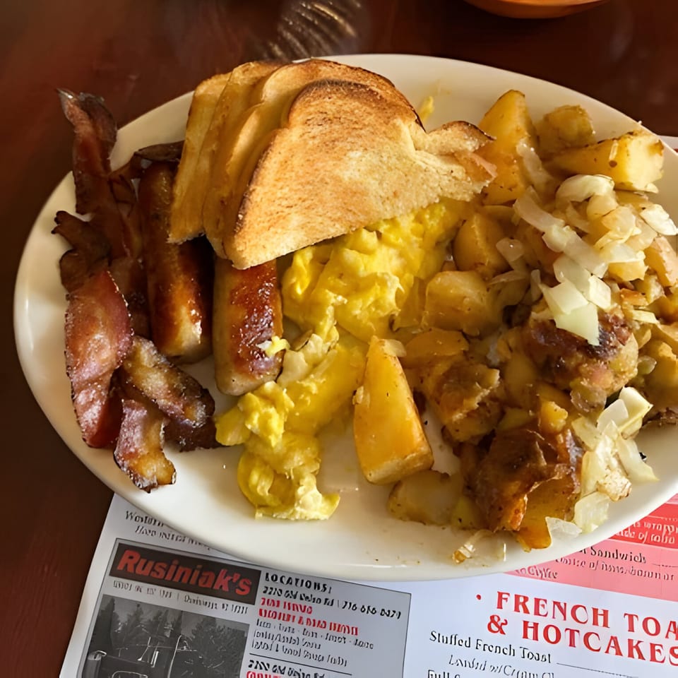 A Polish Villa breakfast plate with scrambled eggs, bacon, sausage, home fries with onions, and toast.