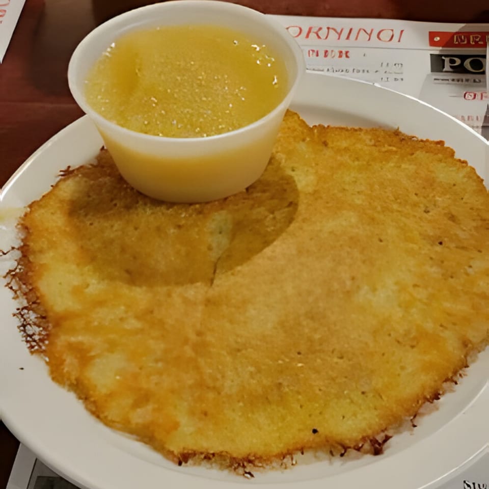 A golden-brown Polish potato pancake with a side of applesauce in a white cup.